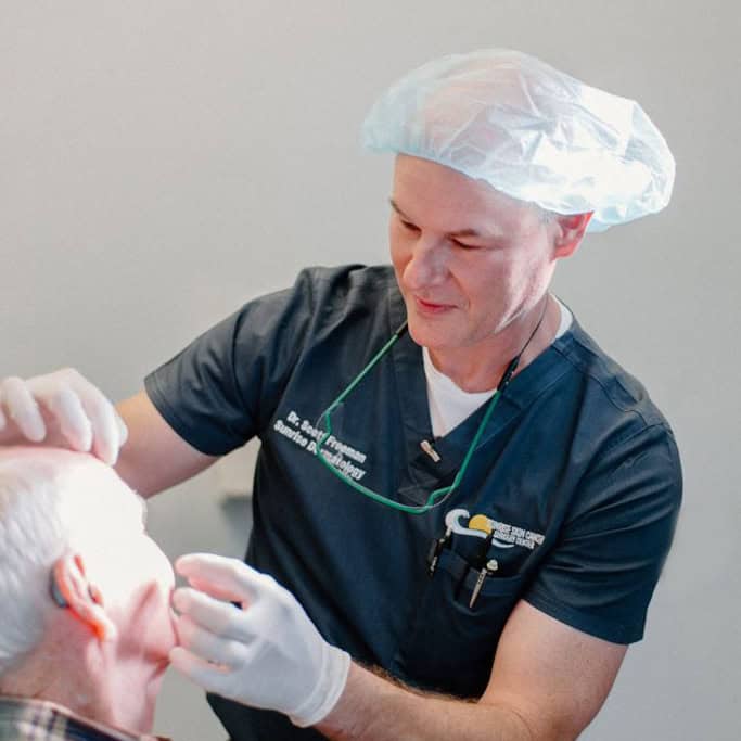 Dr. Scott Freeman examines the skin of an older male patient at Sunrise Dermatology